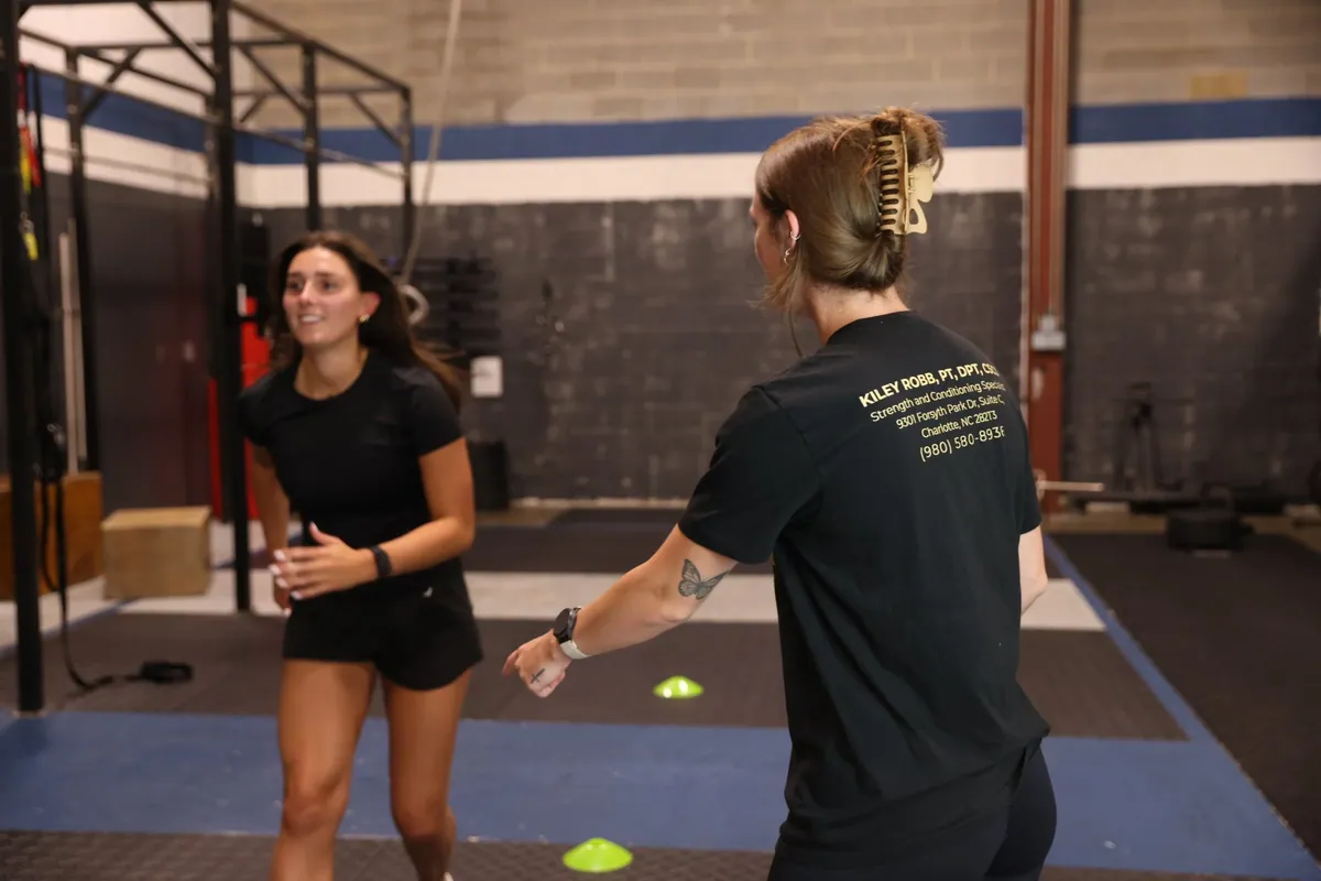 Kiley Robb, PT, DPT, seen from behind, coaches an athlete through a cone drill