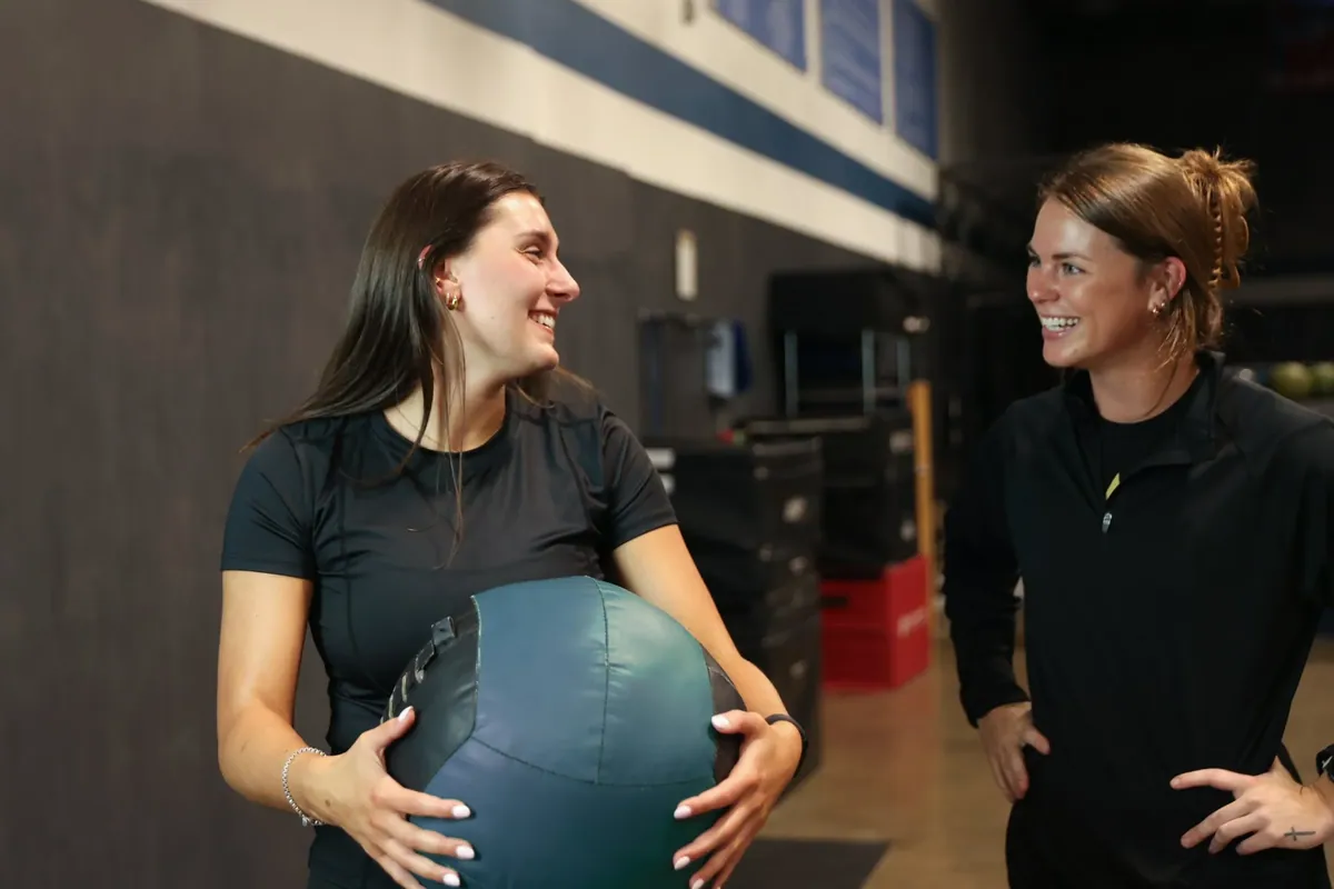 An athlete holds a medicine ball and laughs with Kiley Robb, PT, DPT, during a session